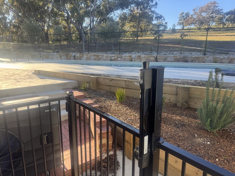 Pool gate latch mounted high on the gate post of a black tubular barrier