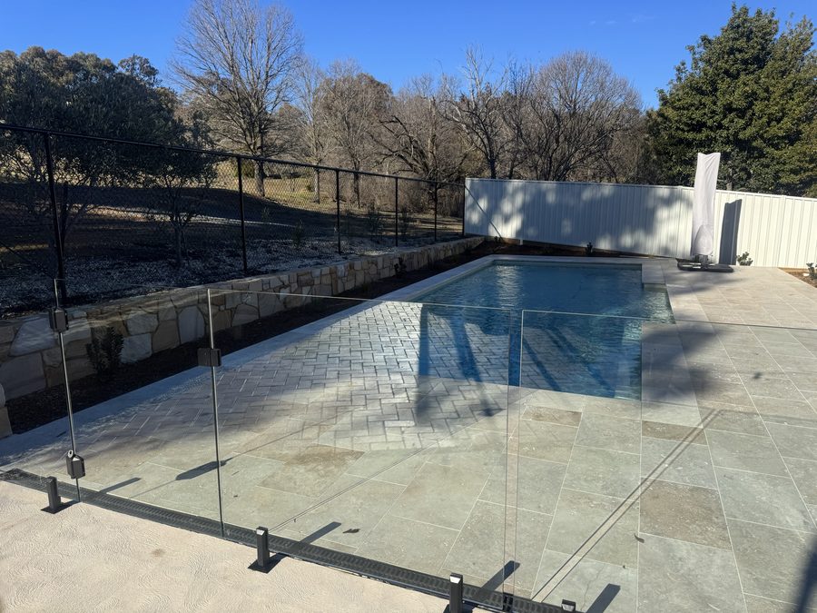 Frameless glass barrier with a Colorbond boundary fence and sandstone retaining wall behind it