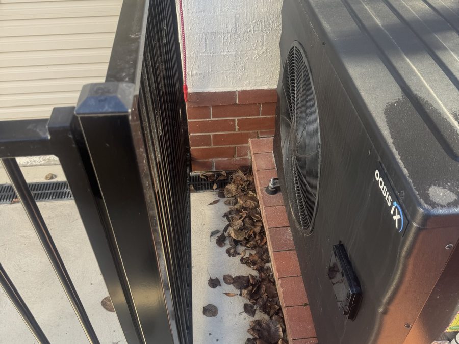 Pool heat pump installed directly against a tubular barrier and brick wall