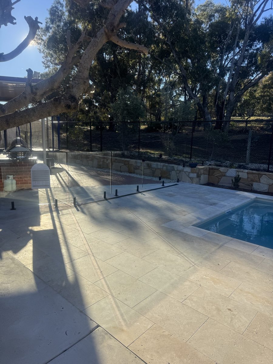 Frameless glass pool barrier under a mature gum, with a sandstone retaining wall behind