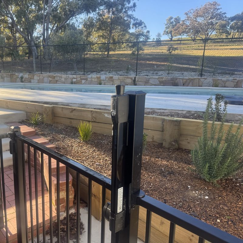 Black tubular pool gate with a vertical latch mounted on the gate post