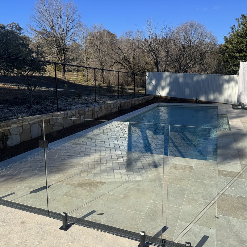 Frameless glass barrier running along a tiled pool surround