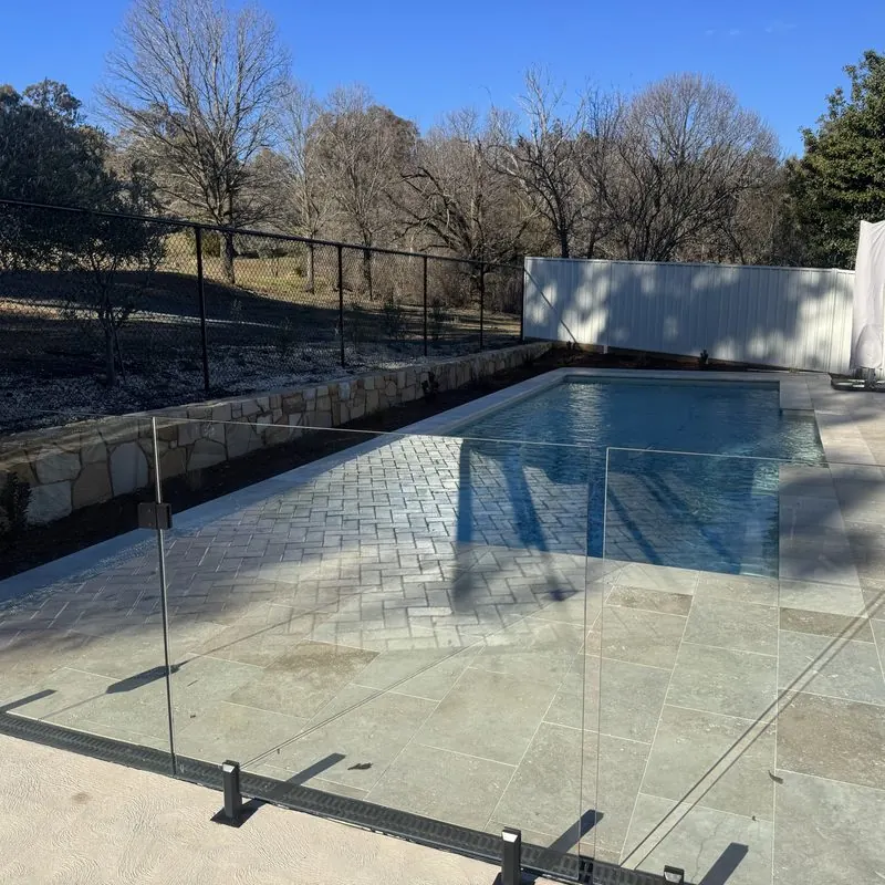Frameless glass barrier running along a tiled pool surround